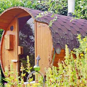 Passt sich schön in die begrünte Gartenecke ein: Die kleine Fass-Sauna bietet Platz für vier Personen.